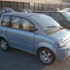 Niebieski, miejski samochód, który może być idealnym pierwszym autem od 16 lat. Stoi na parkingu obok innych pojazdów.