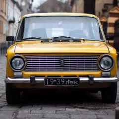 Żółty klasyk z tablicą "19:39 ЛВК" na brukowanej ulicy. RPR rejestracja czeka na swoją kolej.