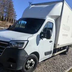 Biały bus z zabudową typu bliźniak, zaparkowany na żwirowym podjeździe.