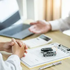 Dwie osoby przy biurku omawiają umowę, na której leżą kluczyki i miniaturowy samochód. Możliwa epuap rejestracja pojazdu online.