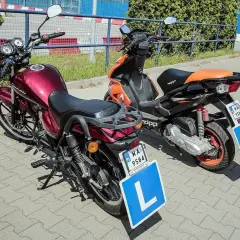 Dwa pojazdy, motocykl i skuter, gotowe do nauki jazdy. Na tablicach literka "L" symbolizuje przyszłych kierowców z prawem jazdy AM.