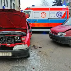 Wypadek po wymuszeniu pierwszeństwa. Dwa czerwone samochody po kolizji, obok karetka pogotowia.