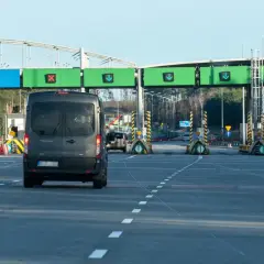 Czarny van zbliża się do bramek autostradowych z zielonymi znakami kierunkowymi.