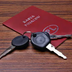 Kluczyki samochodowe leżą na czerwonej karcie pojazdu z napisem "KARTA POJAZDU" i symbolem "PL".