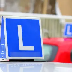 Tablica z literą "L" na dachu samochodu, symbolizująca naukę jazdy. Chcesz wiedzieć, jak zapisać się na prawo jazdy?