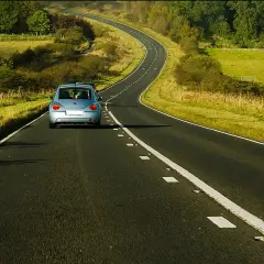 Błękitny Volkswagen Beetle jedzie krętą drogą przez zielone pola. Uważaj na punkty, za ile punktów zabierają prawo jazdy!