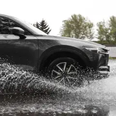 Ciemny samochód SUV z impetem wjeżdża w głęboką kałużę, powodując efektowny aquaplaning i rozbryzgując wodę na boki.