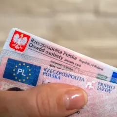 Dłoń trzyma polski dowód osobisty i prawo jazdy. Ważność prawa jazdy jest kluczowa dla swobodnego poruszania się po drogach.