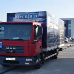 Czerwona ciężarówka MAN z literą "L" na masce, przygotowana do egzaminu na prawo jazdy kategorii C+E. Na naczepie logo WORD.