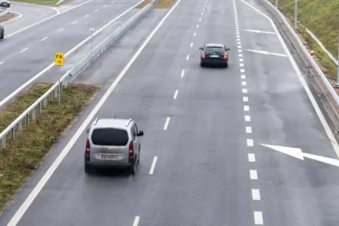 Samochody jadące autostradą. Po lewej stronie widać znak "PA 10" i barierki. Droga ma pas rozbiegowy.