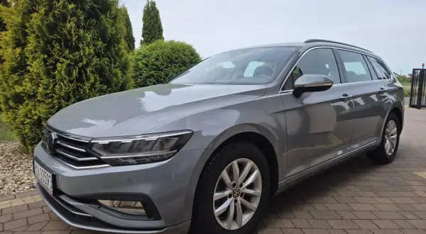 Szary Volkswagen Passat Variant z polskimi tablicami rejestracyjnymi stoi na podjeździe z kostki brukowej, otoczony zielenią.