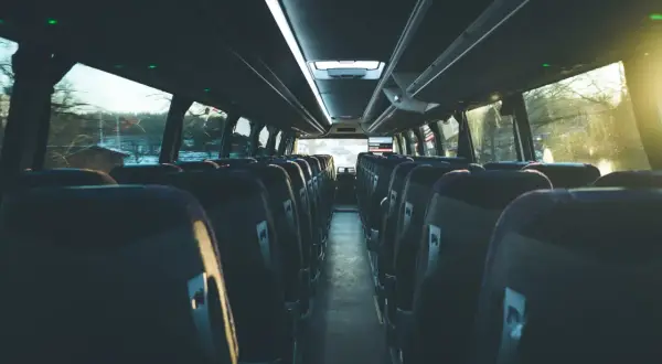 Puste siedzenia w autobusie, gotowe na podróż. Widać rząd siedzeń po obu stronach, sugerując, że busy są wieloosobowe.
