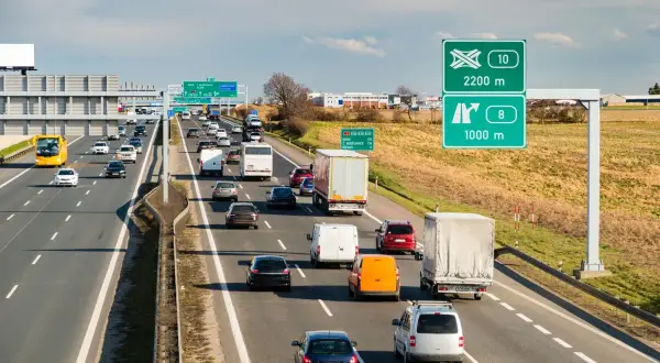 Ruchliwa autostrada w Czechach, z wieloma samochodami i ciężarówkami. Zielone znaki drogowe wskazują kierunki i odległości.