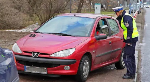 Policjantka kontroluje czerwony samochód. Czy można jeździć bez plastiku po zdaniu egzaminu?