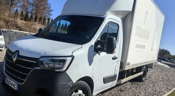 Biały bus z zabudową typu bliźniak, zaparkowany na żwirowym podjeździe.