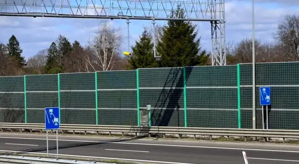 Znak informuje o odcinkowym pomiarze prędkości S5. Za zieloną barierą dźwiękochłonną widać drzewa i niebo.