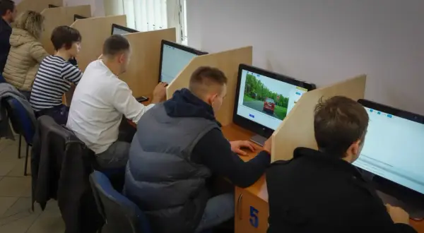 Ludzie siedzą przy komputerach, rozwiązując testy. Tak sprawdzisz, jak zdałeś egzamin teoretyczny na prawo jazdy.