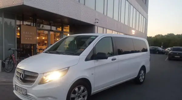Biały bus przed hotelem Arche. Sprawdź nasz wynajem busa z kierowcą cennik dla komfortowych podróży.