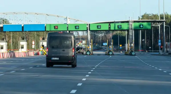 Czarny van zbliża się do bramek autostradowych z zielonymi znakami kierunkowymi.