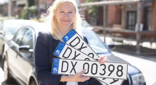 Kobieta trzyma tablice rejestracyjne z numerem DX 00398. Ułatwia to sd rejestracja.