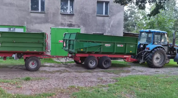 Ciągnik rolniczy z przyczepą, gotowy do pracy w kategorii B+E. Zielone przyczepy czekają na załadunek.
