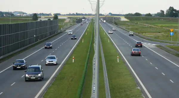 Ruch na drogach szybkiego ruchu w Polsce. Samochody poruszają się po wielopasmowej autostradzie, otoczonej zielenią i ekranami akustycznymi.