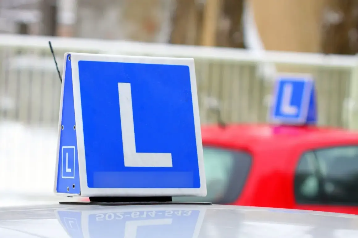 Tablica z literą "L" na dachu samochodu, symbolizująca naukę jazdy. Chcesz wiedzieć, jak zapisać się na prawo jazdy?