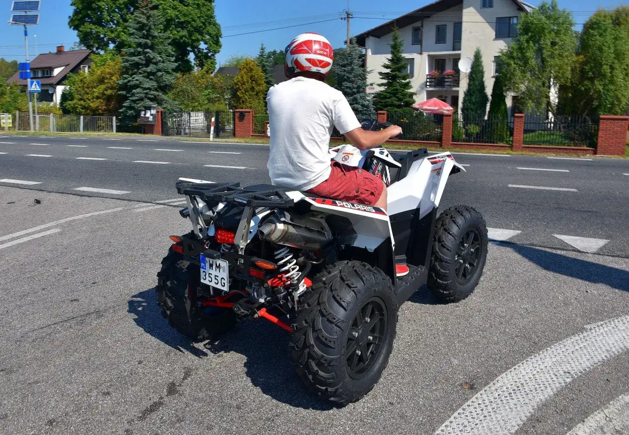 Mężczyzna w kasku jedzie quadem po drodze. Posiada prawo jazdy AM, więc może legalnie poruszać się tym pojazdem.