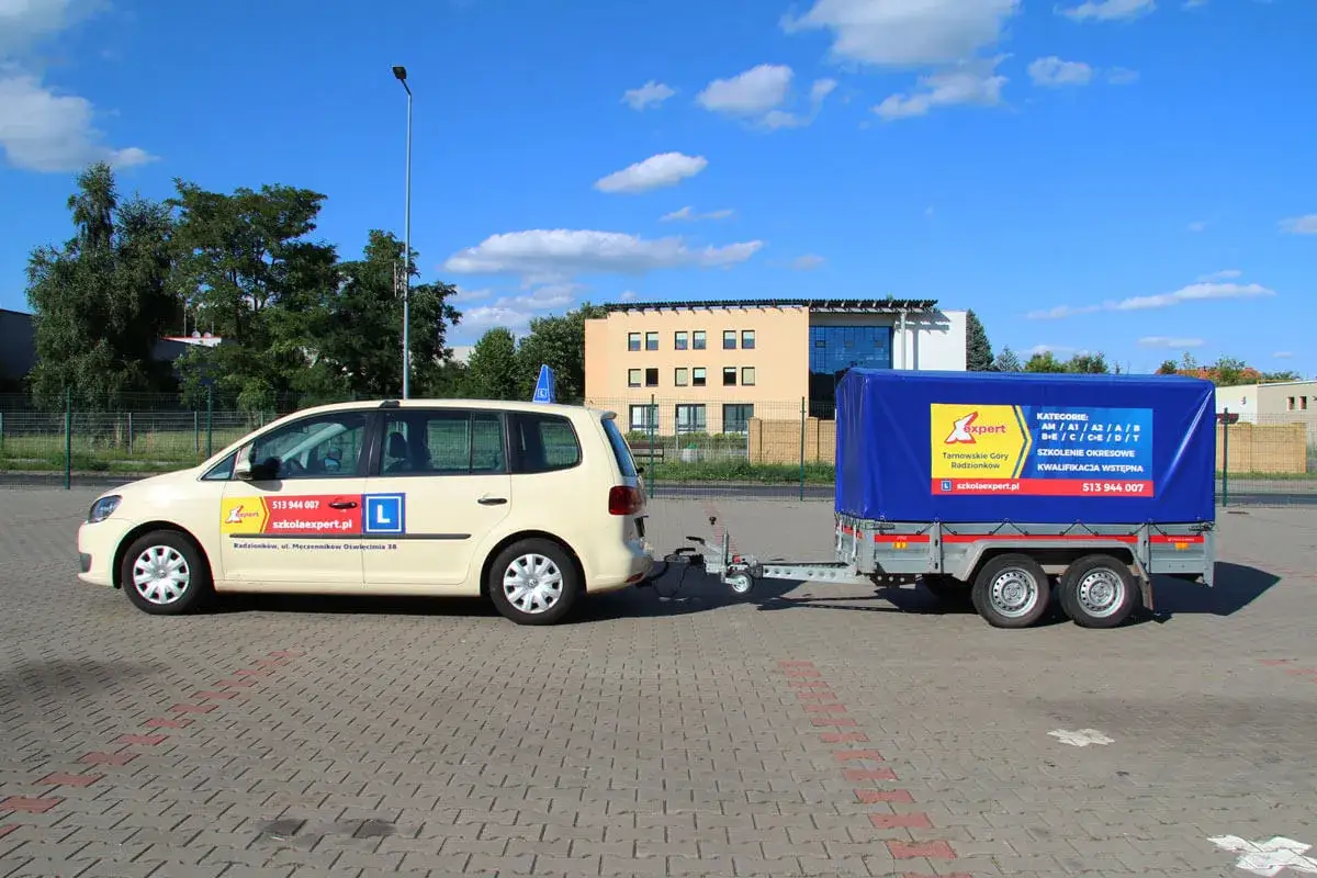 Samochód nauki jazdy z przyczepą, gotowy do szkolenia kategorii B. Na przyczepie logo szkoły jazdy i lista kategorii.