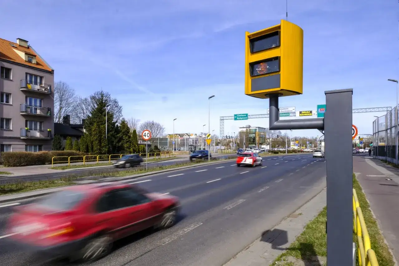 Nowe fotoradary czuwają nad ruchem na drodze. Samochody pędzą, a żółta skrzynka monitoruje prędkość.