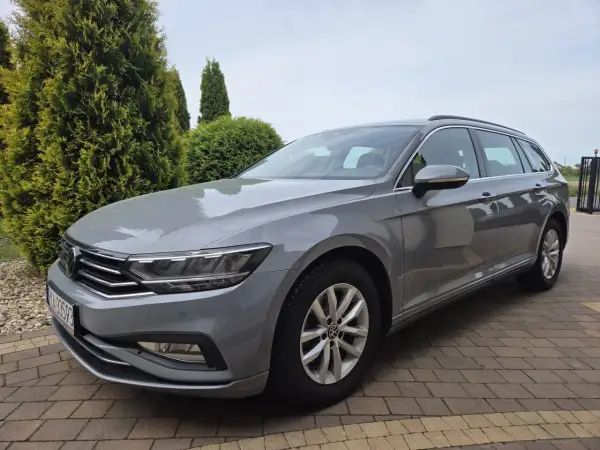 Szary Volkswagen Passat Variant z polskimi tablicami rejestracyjnymi stoi na podjeździe z kostki brukowej, otoczony zielenią.