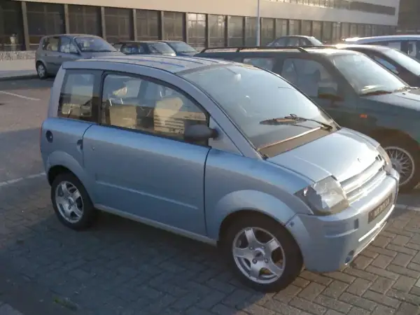Niebieski, miejski samochód, który może być idealnym pierwszym autem od 16 lat. Stoi na parkingu obok innych pojazdów.