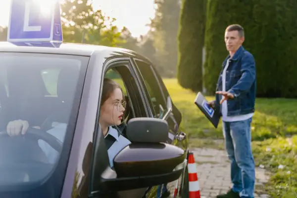 Młoda kobieta w okularach uczy się jeździć pod okiem instruktora. Widać, ile ważny jest kurs na prawo jazdy dla pewności siebie za kierownicą.