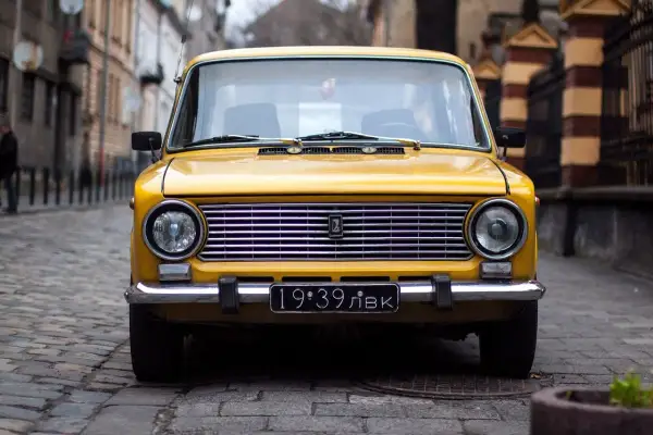 Żółty klasyk z tablicą "19:39 ЛВК" na brukowanej ulicy. RPR rejestracja czeka na swoją kolej.