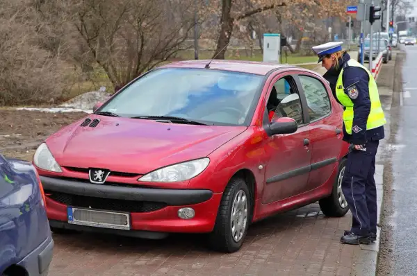 Policjantka kontroluje czerwony samochód. Czy można jeździć bez plastiku po zdaniu egzaminu?