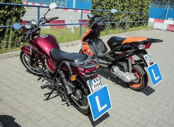Dwa pojazdy, motocykl i skuter, gotowe do nauki jazdy. Na tablicach literka "L" symbolizuje przyszłych kierowców z prawem jazdy AM.