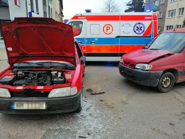 Wypadek po wymuszeniu pierwszeństwa. Dwa czerwone samochody po kolizji, obok karetka pogotowia.