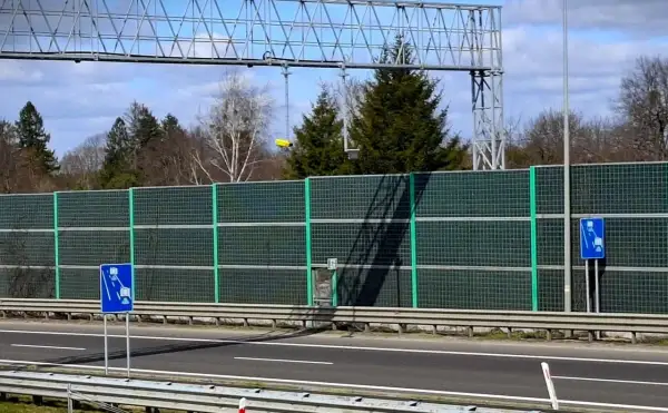 Znak informuje o odcinkowym pomiarze prędkości S5. Za zieloną barierą dźwiękochłonną widać drzewa i niebo.