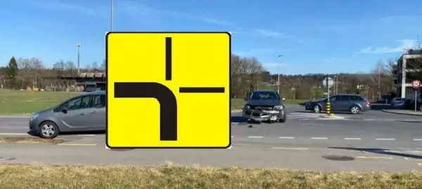 Znak drogowy informuje, kto ma pierwszeństwo na skrzyżowaniu równorzędnym. Widać uszkodzone auto po wypadku.