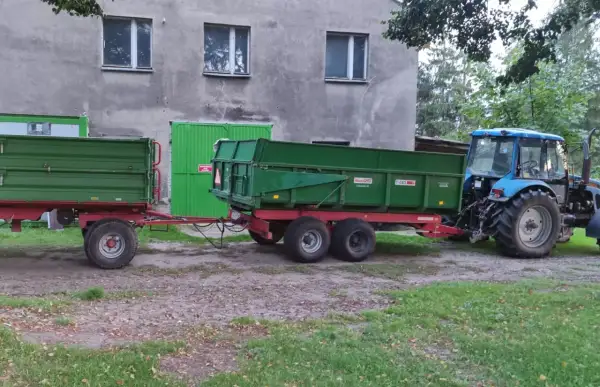 Ciągnik rolniczy z przyczepą, gotowy do pracy w kategorii B+E. Zielone przyczepy czekają na załadunek.
