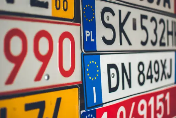 Zbliżenie na stos tablice rejestracyjne państw. Widać numery i litery, m.in. PL, SK, DN.