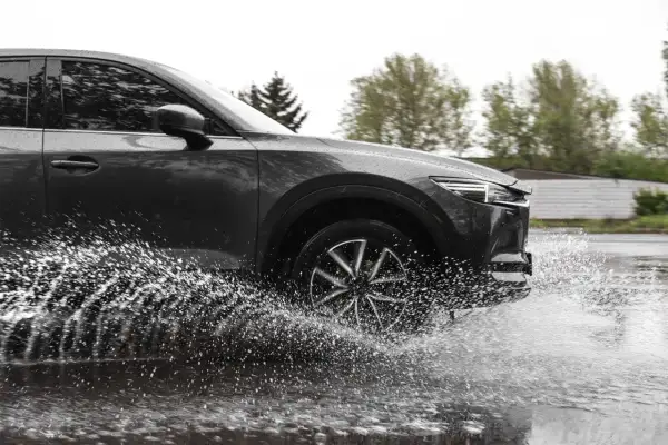 Ciemny samochód SUV z impetem wjeżdża w głęboką kałużę, powodując efektowny aquaplaning i rozbryzgując wodę na boki.