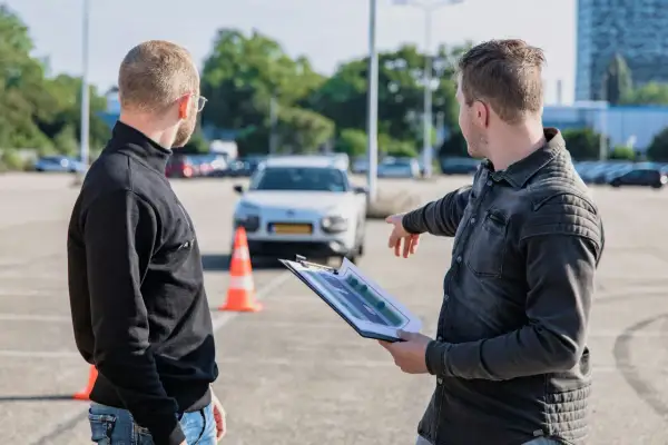 Instruktor pokazuje kursantowi plan placu manewrowego, omawiając, ile błędów można zrobić na egzaminie teoretycznym na prawo jazdy.