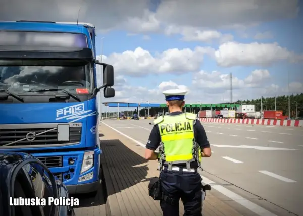Policjant w kamizelce odblaskowej przy niebieskiej ciężarówce Volvo FH13. W tle przejście graniczne, kategoria c.