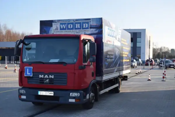 Czerwona ciężarówka MAN z literą "L" na masce, przygotowana do egzaminu na prawo jazdy kategorii C+E. Na naczepie logo WORD.